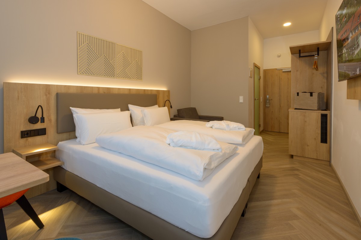 Modernes Hotelzimmer im Hotel Bodenmais mit großem Bett, Holzmöbeln, minimalistischem Dekor und warmer Beleuchtung.