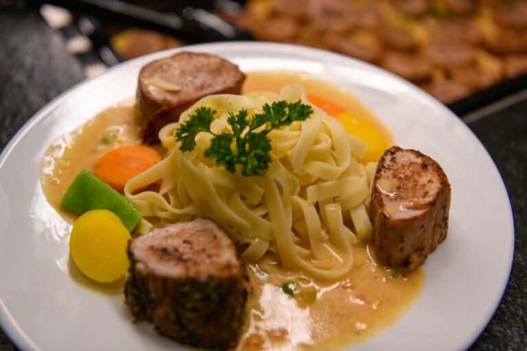 Genießen Sie einen Teller Pasta mit gegrilltem Fleisch, Sahnesauce, buntem Gemüse und Petersiliengarnitur – ein kulinarischer Hochgenuss, der an die exquisiten Speiseerlebnisse im Hotel Bodenmais erinnert.