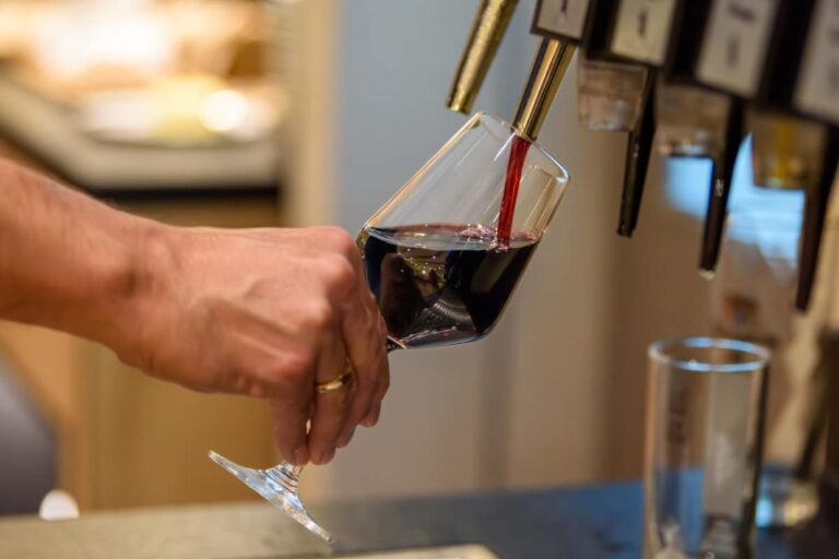 Im eleganten Ambiente des Hotels Bodenmais gießt eine Hand anmutig Rotwein aus einem Spender in ein Glas und fängt damit die Essenz raffinierten Genusses ein.