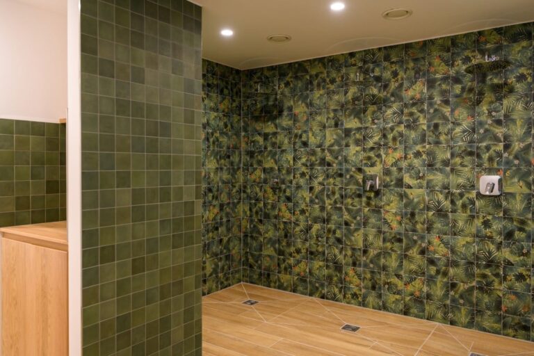 Erleben Sie die Ruhe einer Spa-ähnlichen Oase im Hotel Bodenmais mit einem Duschbereich, der mit grünen botanischen Fliesen geschmückt und durch einen warmen Holzboden und beruhigende Deckenbeleuchtung ergänzt wird.