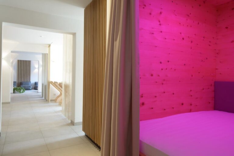 Das moderne Spa-Interieur des Hotel Bodenmais besticht durch eine rosa beleuchtete Nische und ein gemütliches Bett. Der helle Flur und die Holzakzente schaffen eine ruhige Atmosphäre und bieten den perfekten Rückzugsort in Bodenmais.